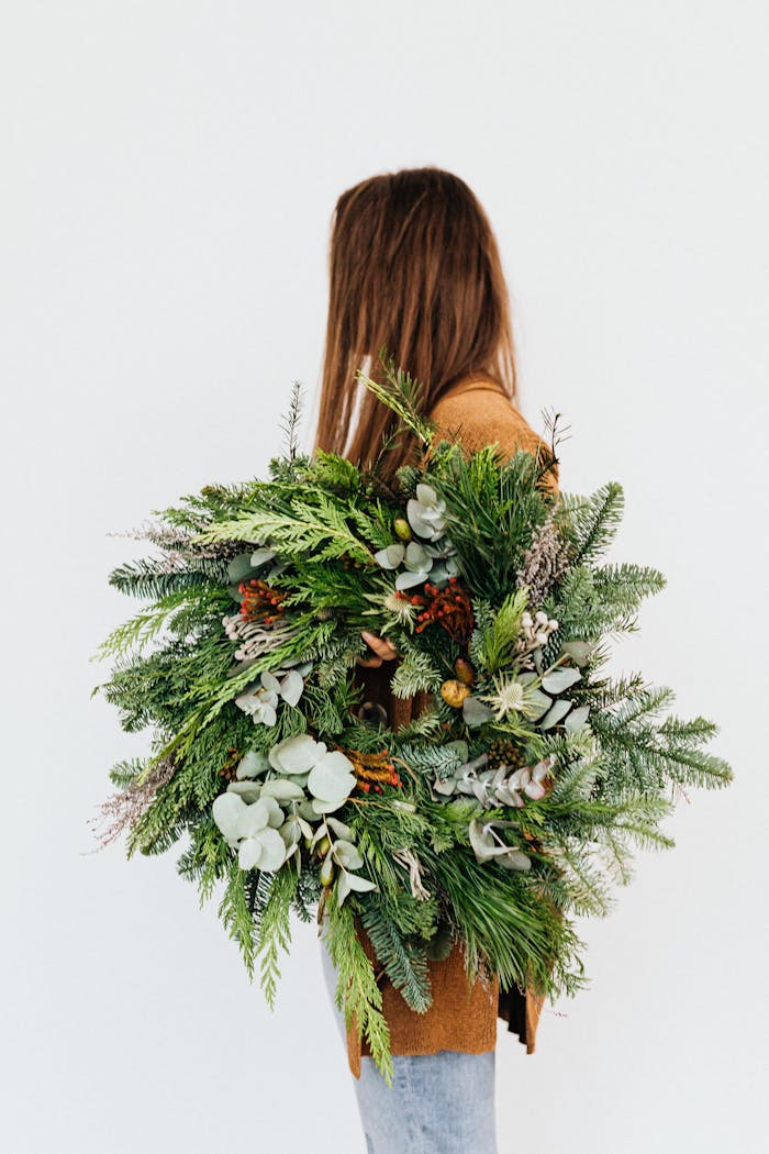 A woman in a brown coat holding a lush evergreen wreath, ideal for Christmas decor.